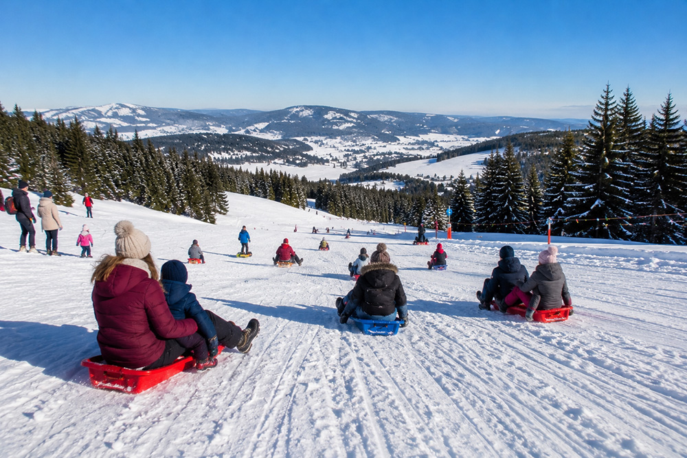 Descente en luge sur une piste enneigée du Haut-Jura avec vue sur les montagnes