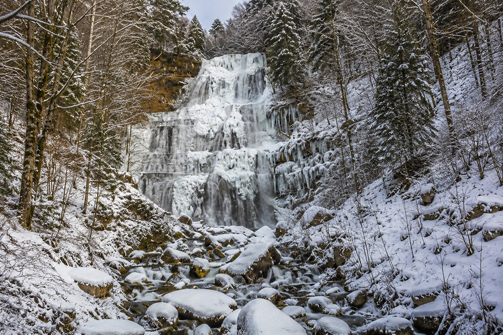 Grande cascade gelée des Cascades du Hérisson entourée de neige et de forêt jurassienne