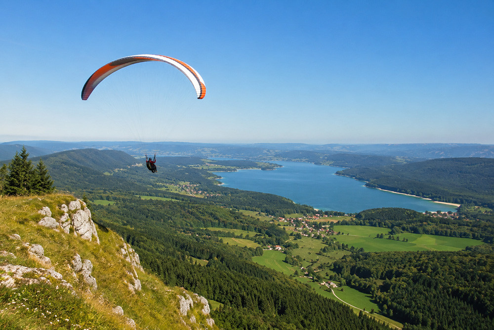 Parapente survolant les montagnes et vallées du Haut-Jura par temps ensoleillé